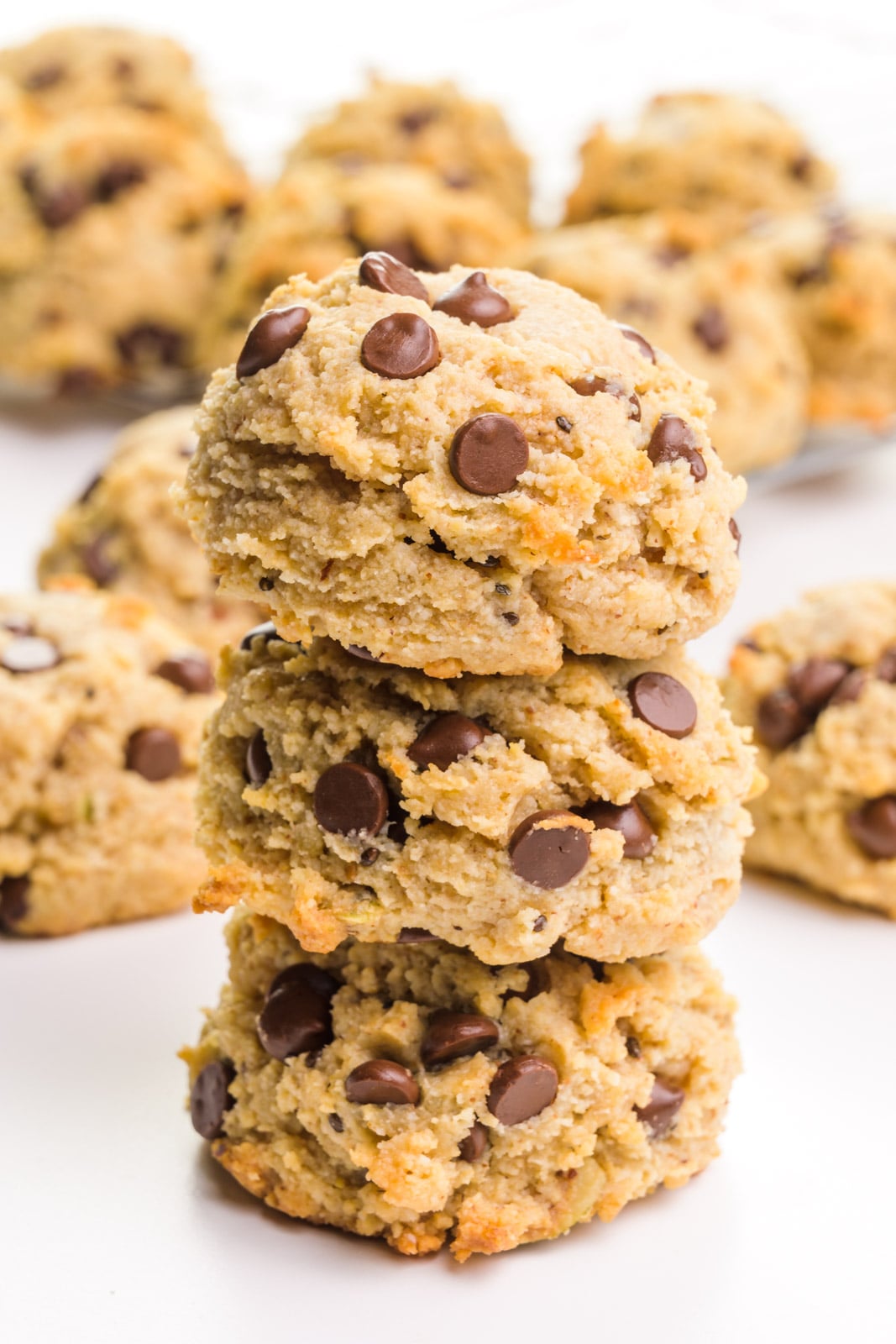 A stack of three almond flour cookies showcase lots of chocolate chips. there are more cookies in the background.