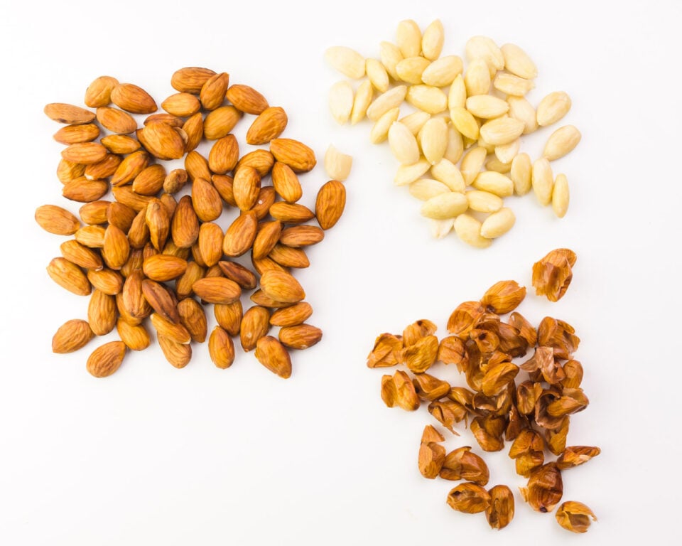 Looking down on almonds, some with the skins on and some that have the skins removed. There's a pie of almond skins next to them.