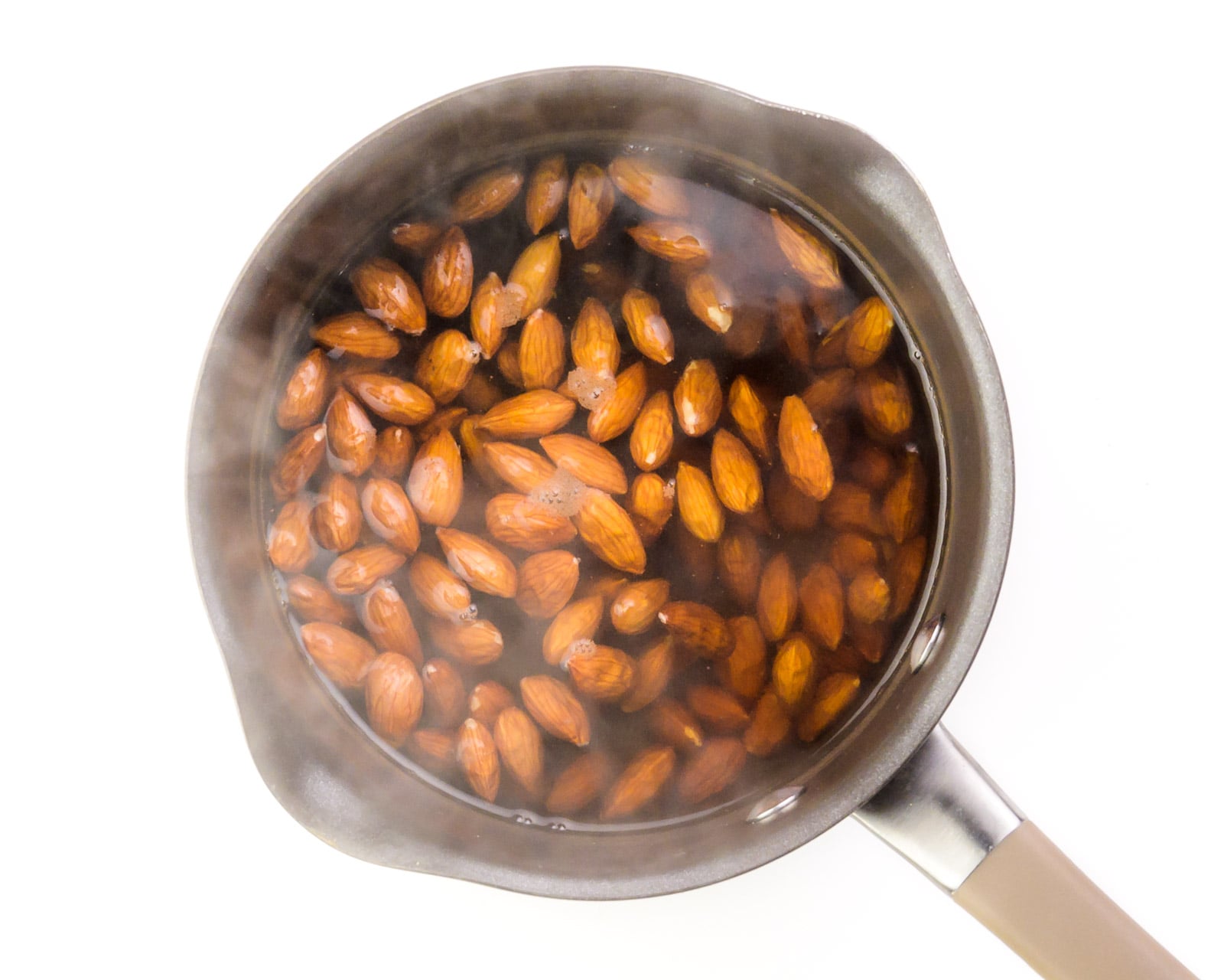 Looking down on a saucepan with raw almonds in boiling water.