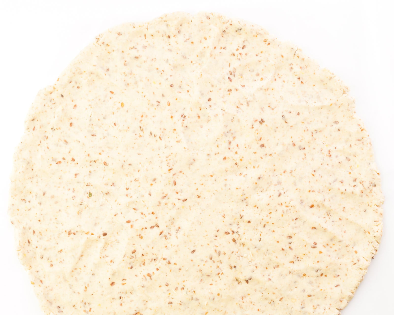 Looking down on an unbaked pizza crust that has been pressed out into a large circle.