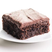 A piece of chocolate zucchini cake sits on a plate. It has frosting on top.