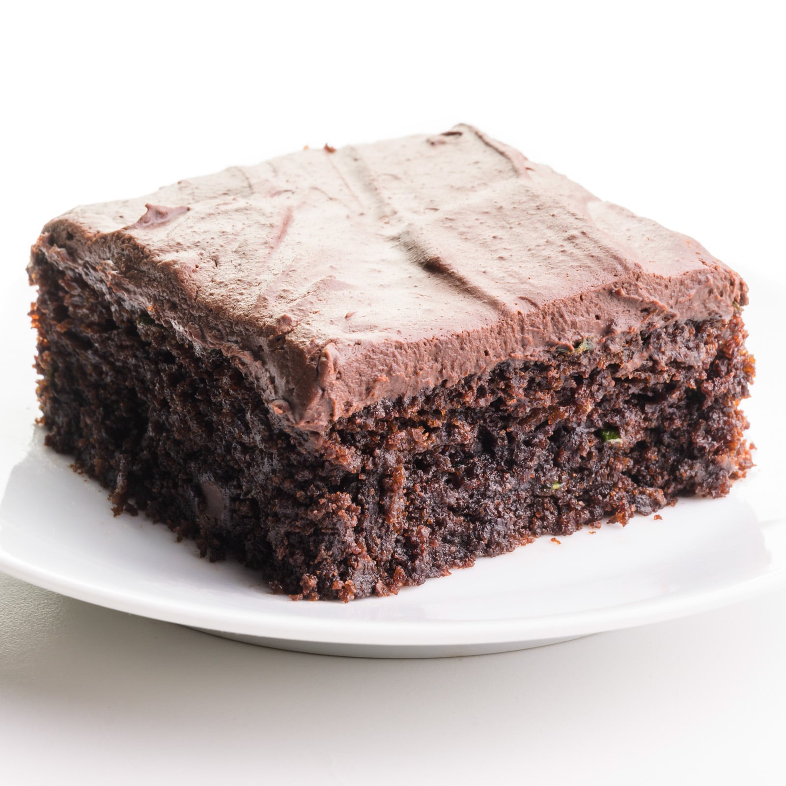 A piece of chocolate zucchini cake sits on a plate. It has frosting on top.