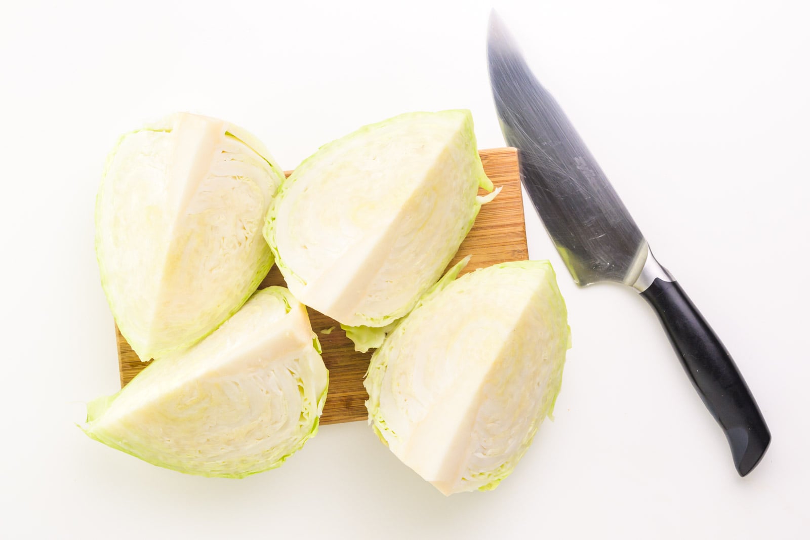 Looking down on four quarters of cabbage on a cutting board with a chef's knife beside it.