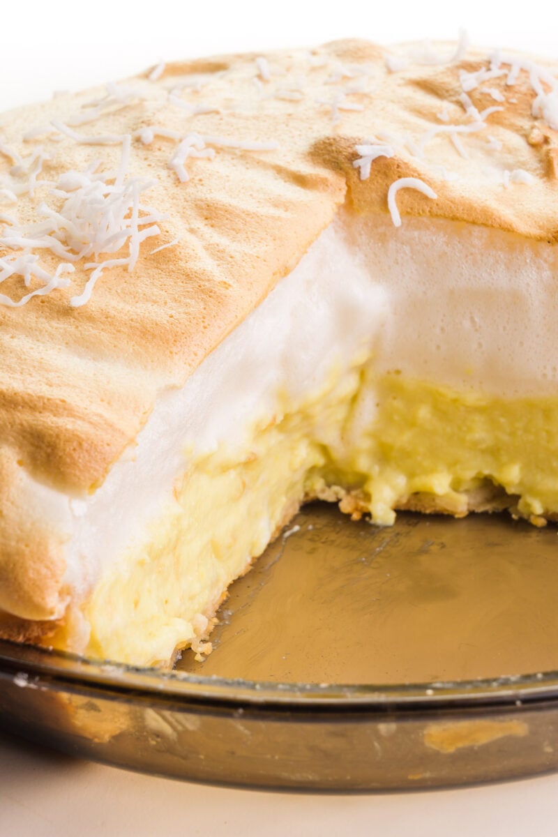 A slice has been cut out of a vegan coconut meringue pie, showing the creamy coconut filling topped with lots of vegan meringue.