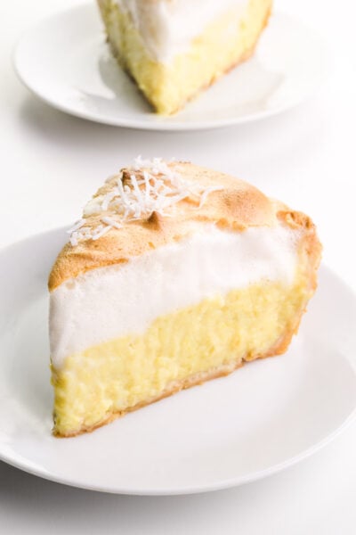 A slice of vegan coconut meringue pie sits on a plate. Another slice is on a plate behind it.
