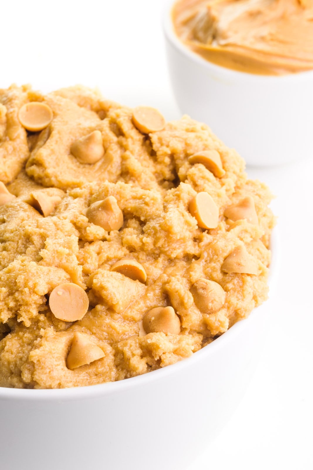 A bowl holds edible peanut butter cookie dough with peanut butter chips. There's a bowl of peanut butter in the background.