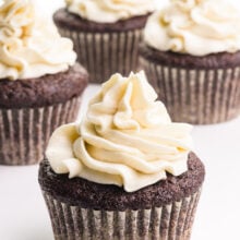 A cupcake has lots of swirly vegan ermine frosting on top. There are three more cupcakes with frosting in the background.