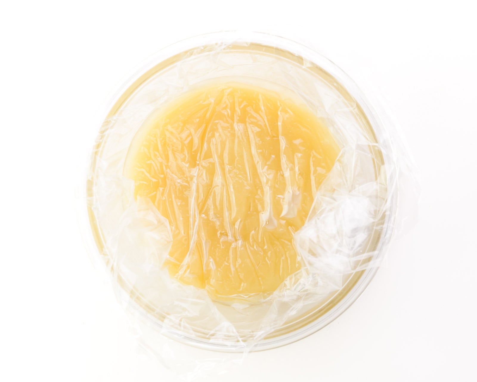 Looking down on a bowl full of a creamy mixture. It's covered in plastic wrap and the wrap has been tucked down into the bowl, touching the creamy mixture.