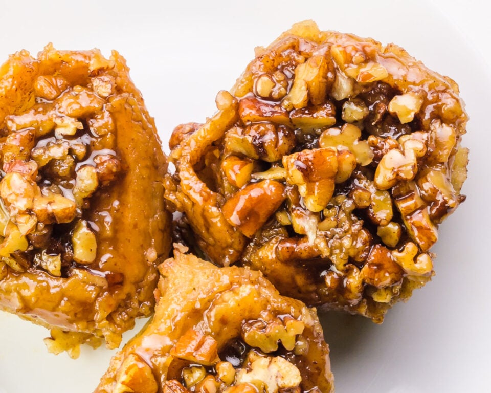Looking down on three sticky buns on a plate. They're topped with chopped pecans.