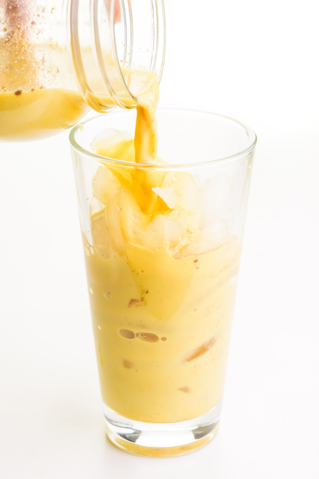 Golden milk is being poured into a glass with ice.