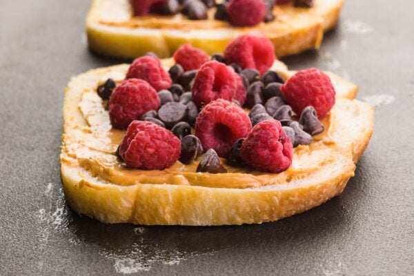 Slices of bread are on a griddle and topped with peanut butter, chocolate chips, and fresh raspberries.