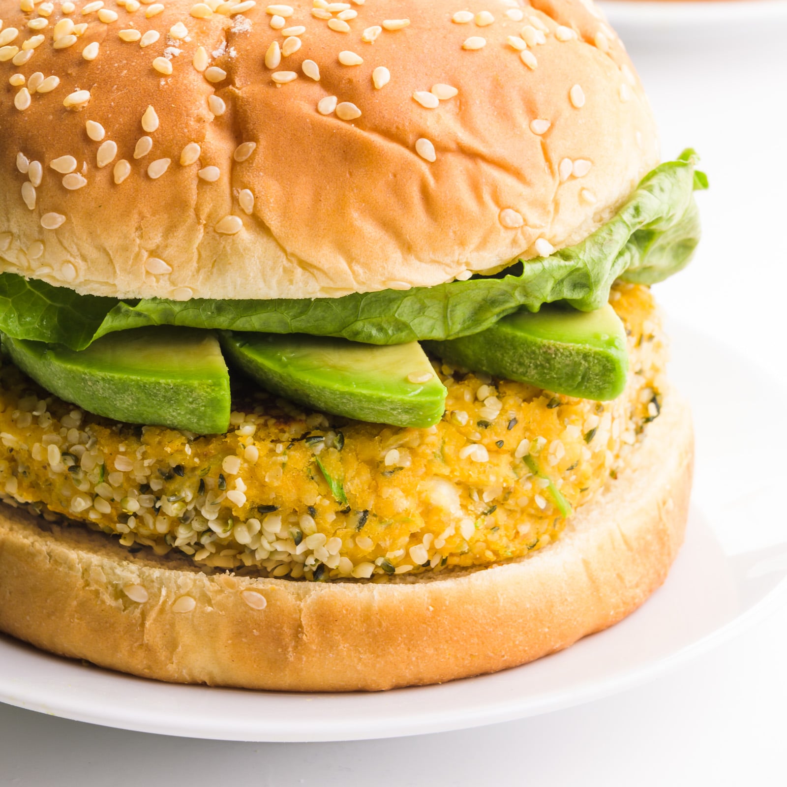 A closeup of a hemp burger on a bun with avocado slices and lettuce.