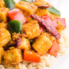A dish of kung pao tofu is served over rice. There is a bowl with more rice in the background.