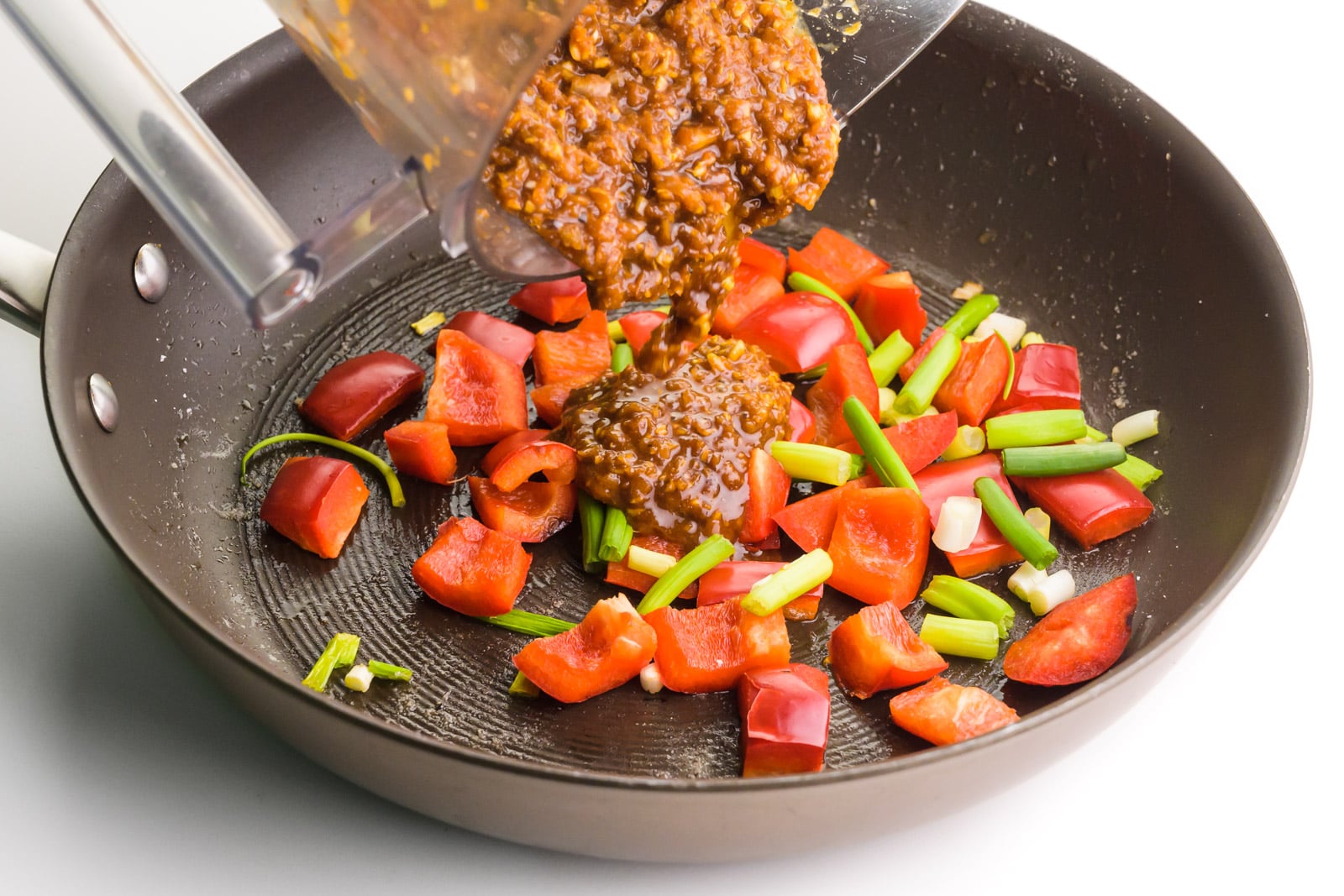 Kung Pao sauce is being poured into a skillet with cooked veggies.