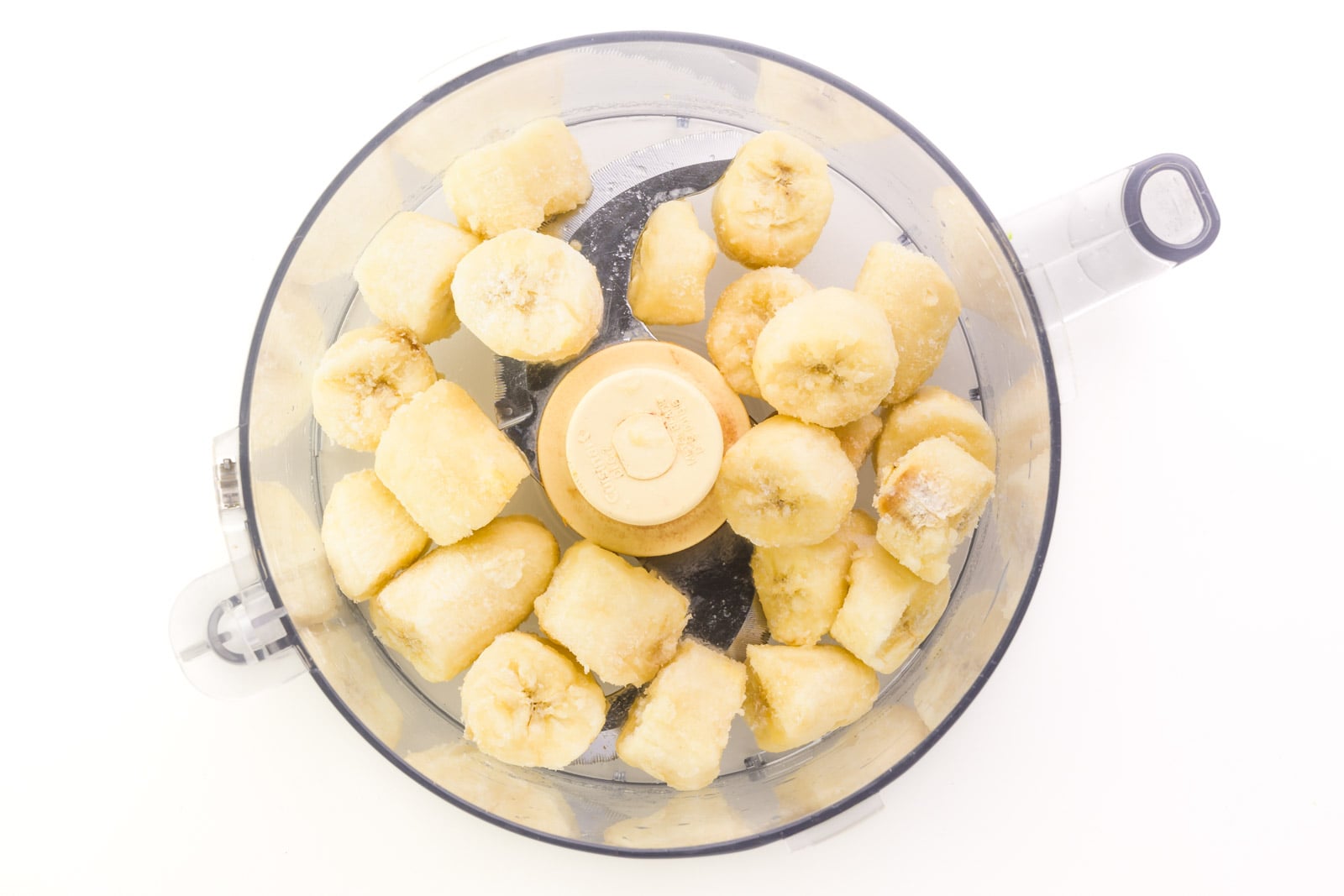Frozen bananas pieces are in the bottom of a food processor bowl.
