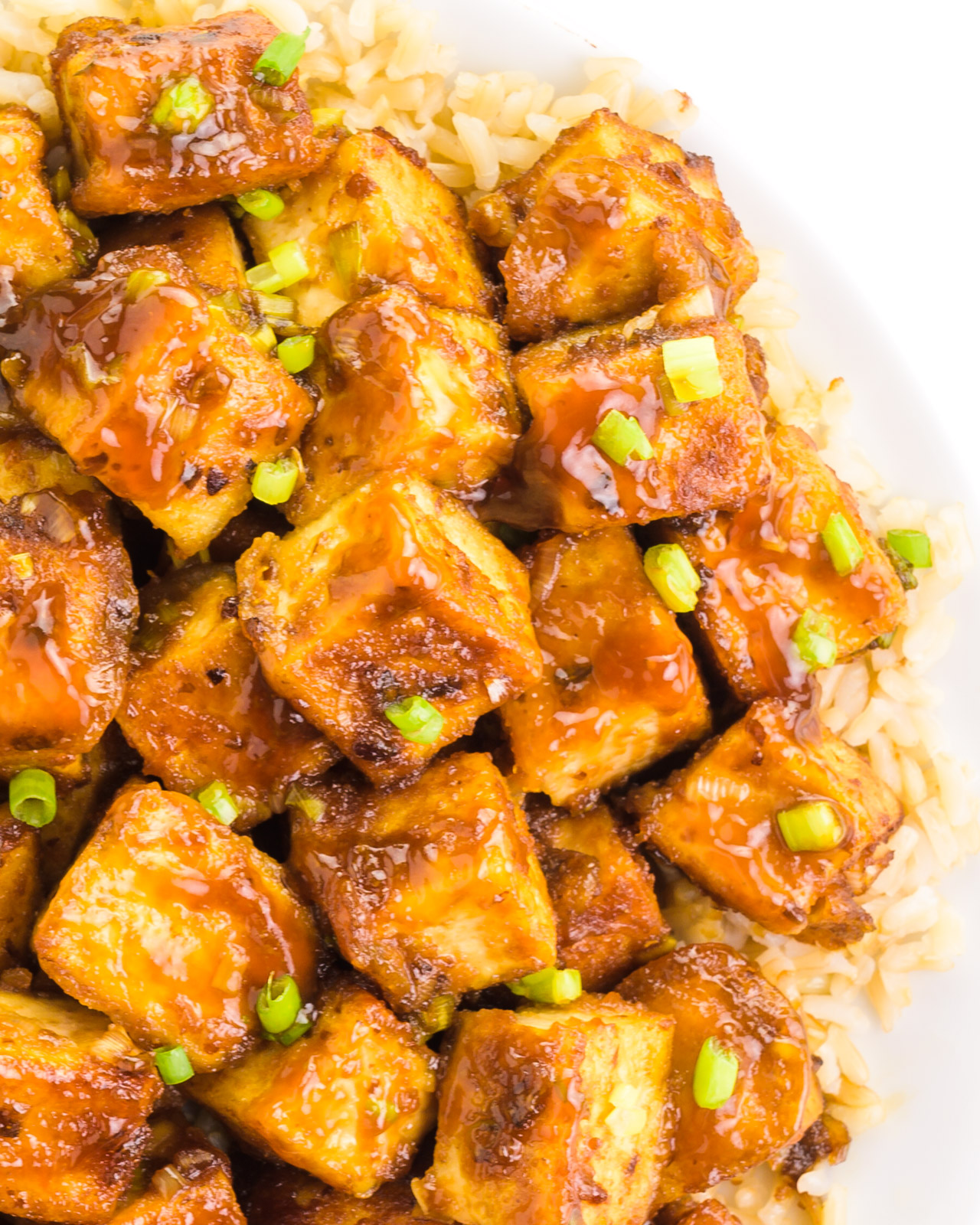 Looking down on a plate of orange tofu on a bed of rice.