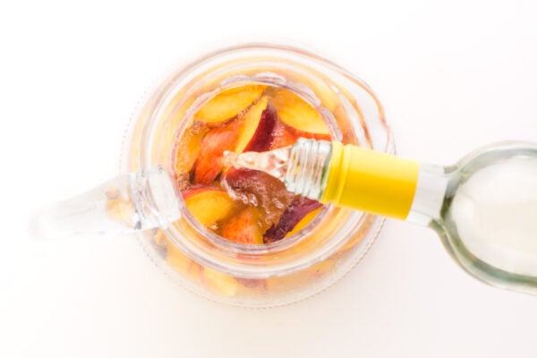 Wine is being poured into a pitcher full of peach slices.