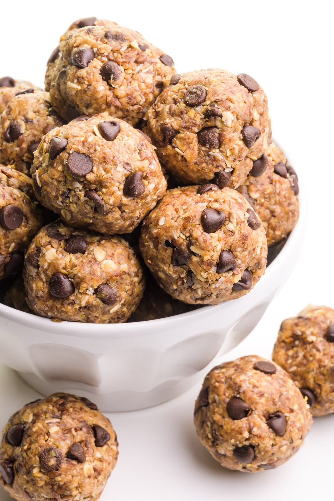 A bowl is full of energy balls and there are more on the table top around the bowl.