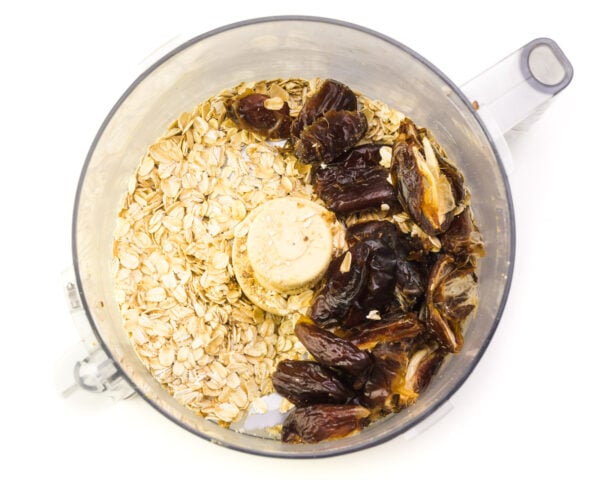 Pitted dates and oats are in the bottom of a food processor bowl waiting to be processed.