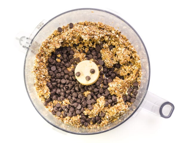 The energy balls meal is in a bottom of a food processor with chocolate chips.