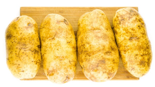 Four potatoes have been picked with a fork, covered with oil, and seasoned with salt and pepper. They are sitting on a cutting board.