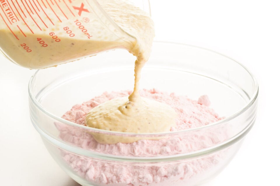 A creamy sauce is being poured into a bowl with strawberry cake mix.