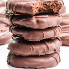 A stack of vegan chocolate mint cookies shows the top one with a bite taken out. There are more cookies in the background.