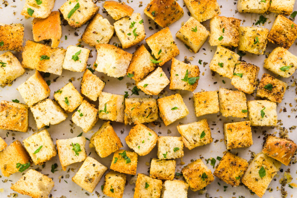 Looking down on a baking tray covered with seasoned croutons.