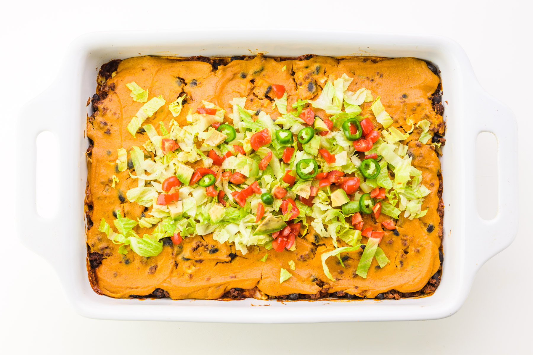 Looking down on a casserole with lots of toppings, like chopped lettuce, tomatoes, and jalapeños.