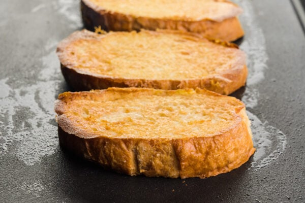 Slices of vegan French toast are cooking on a heated griddle.