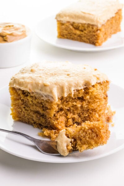 A bite of cake is on a fork sitting on a plate with the rest of the cake. There's another slice of cake and a bowl of peanut butter in the background.