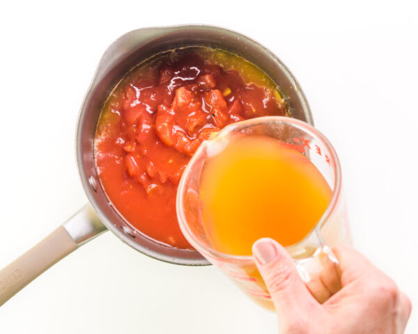Vegetable broth is being poured into a saucepan with tomatoes and other vegetables.