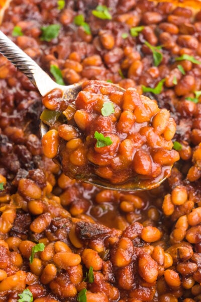 A spoon holds a serving of vegan baked beans hovering over over the rest of the dish full of it.