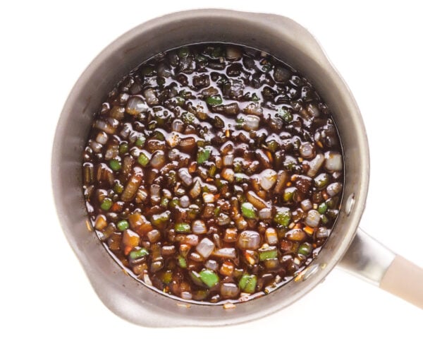 Looking down into a saucepan full of BBQ sauce mixture with chopped onions and green bell peppers.