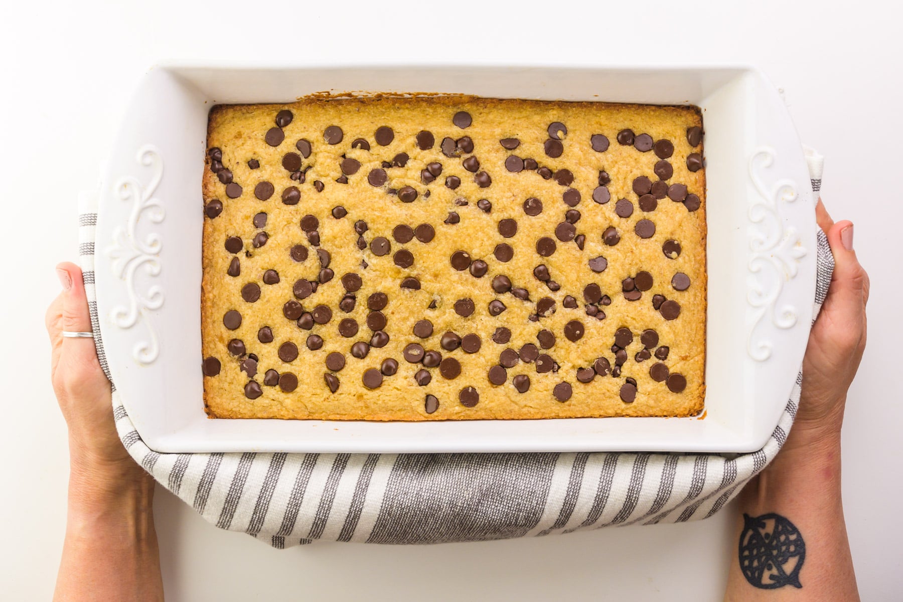 Two hands hold a towel with a pan of blondies fresh from the oven.