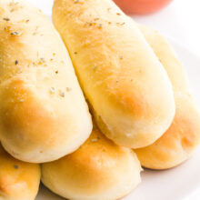 Vegan breadsticks are piled high on a plate sitting in front of a bowl of marinara sauce.