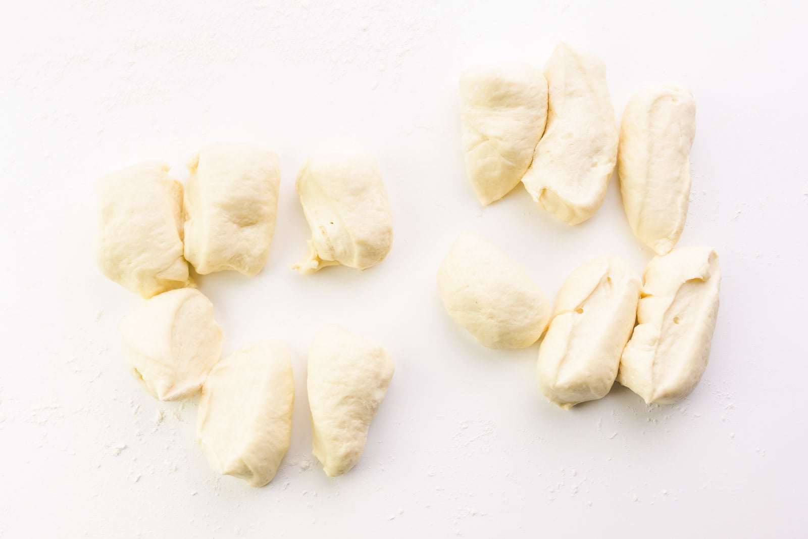 Dough has been cut into 12 pieces. They are sitting on a white counter.