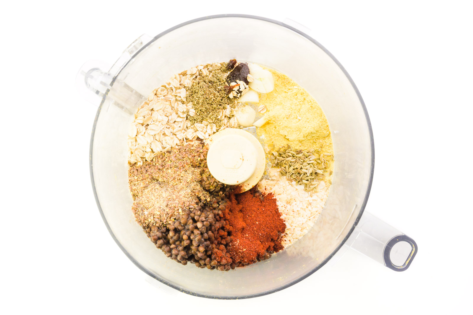 Seasonings, lentils, and other ingredients are at the bottom of a food processor bowl.