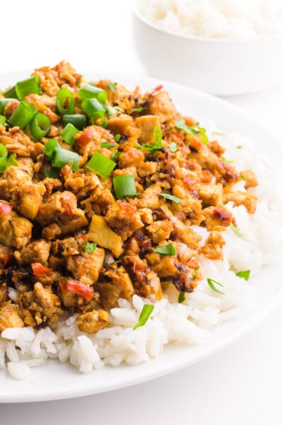 A plate holds rice topped with vegan bulgogi. There are chopped green onions on top and a bowl of rice in the background.