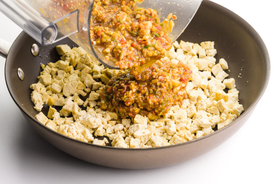 A sauce is being poured over tofu bits in a skillet.