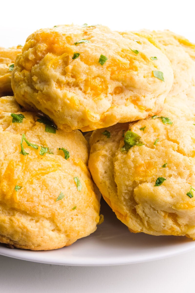 A plate holds several biscuits, showing cheese and flecks of chopped parsley on top.