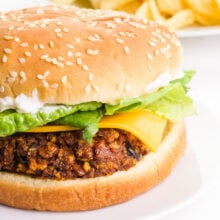 A veggie chorizo burger sits on a plate with potato chips in the background.