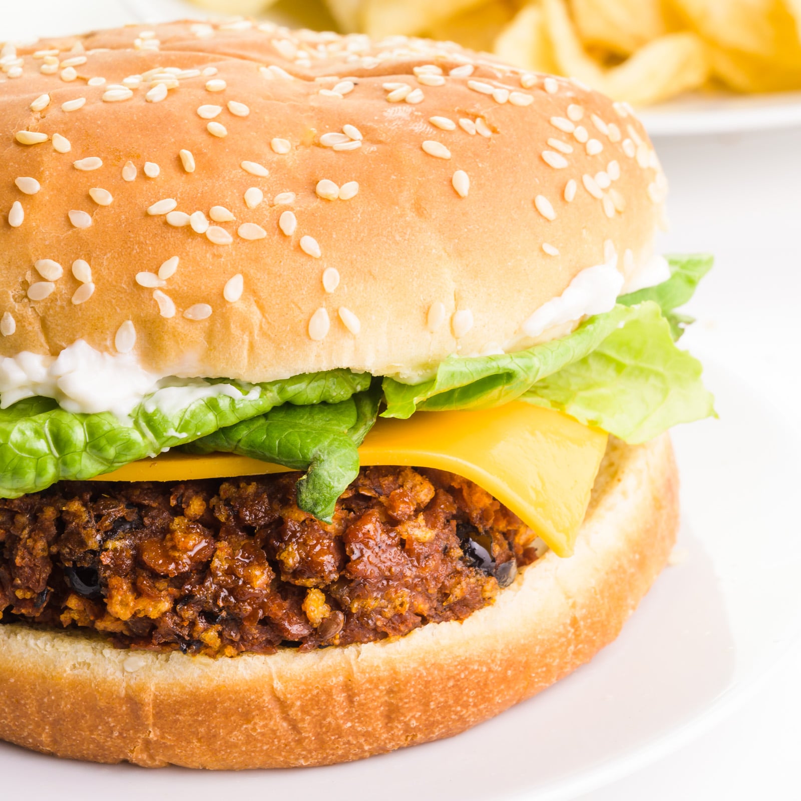 A veggie chorizo burger sits on a plate with potato chips in the background.