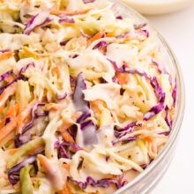 Looking down on the right side of a bowl of coleslaw with a bowl of more coleslaw sauce in the background.