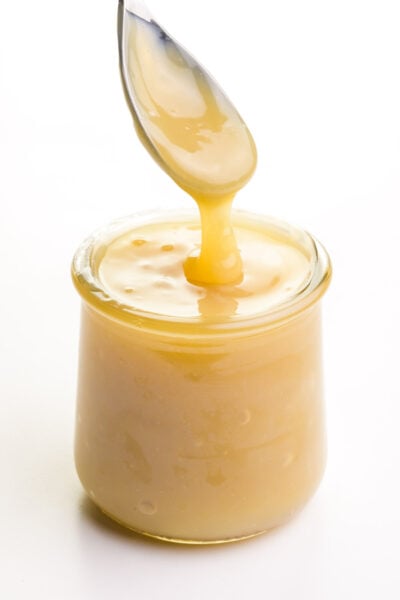 A spoon full of vegan condensed milk hovers over a glass jar full of the mixture.
