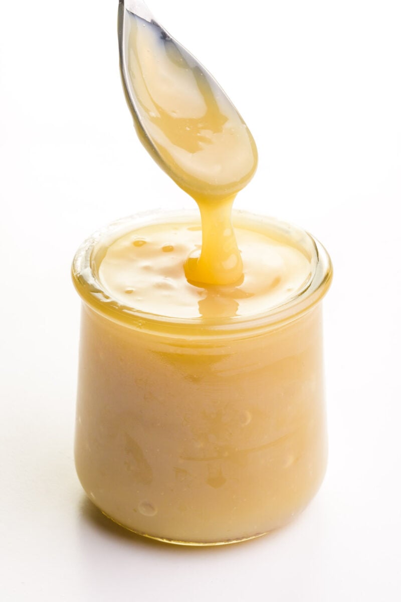 A spoon full of vegan condensed milk hovers over a glass jar full of the mixture.