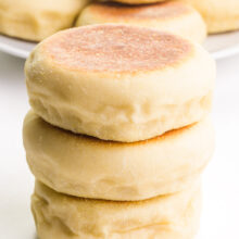 A stack of 3 vegan English muffins is in front of a wire rack with more muffins.