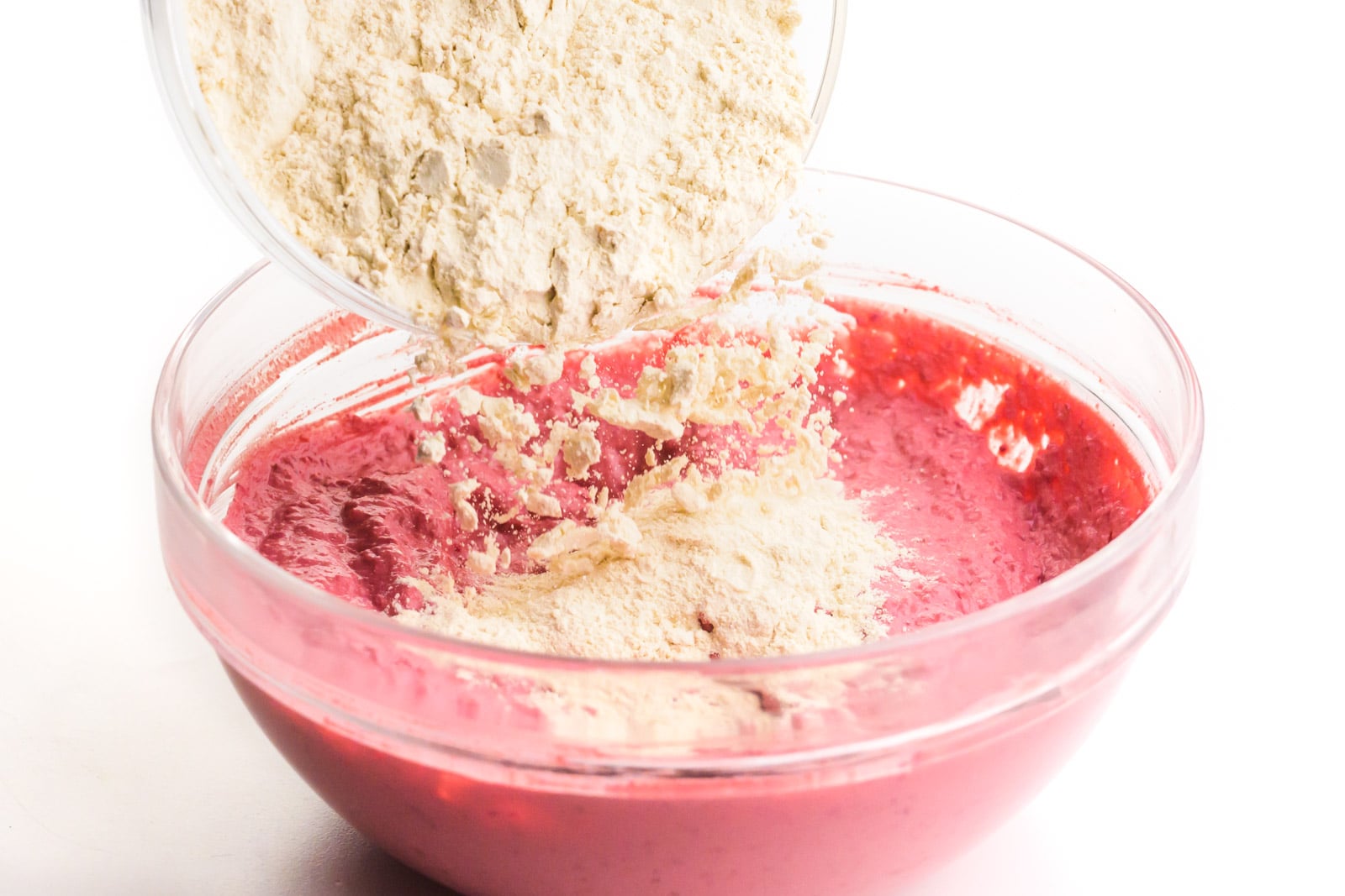 Vital wheat gluten is being poured into a bowl with pink batter.