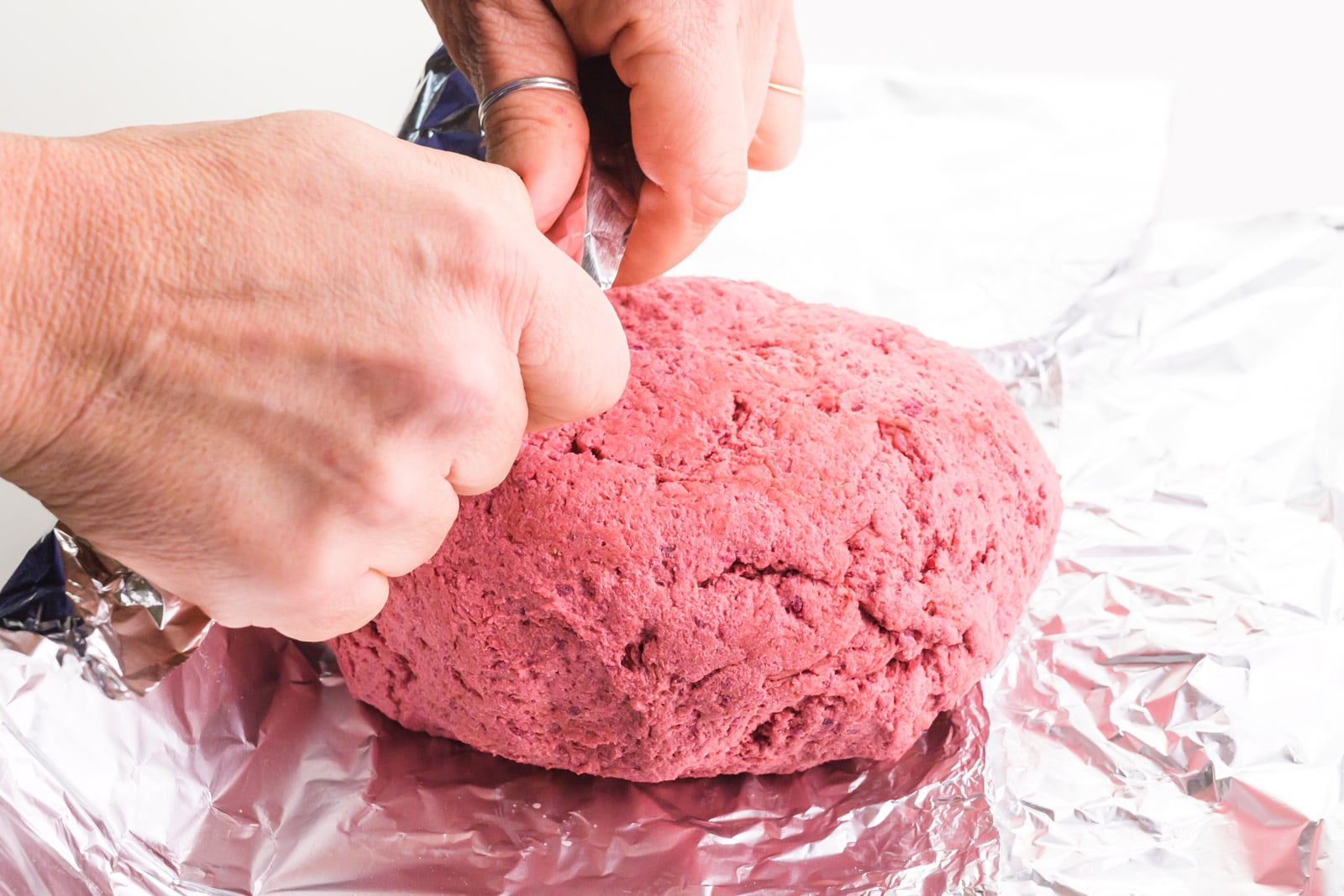 Hands are pulling up aluminum foil over a pink loaf.