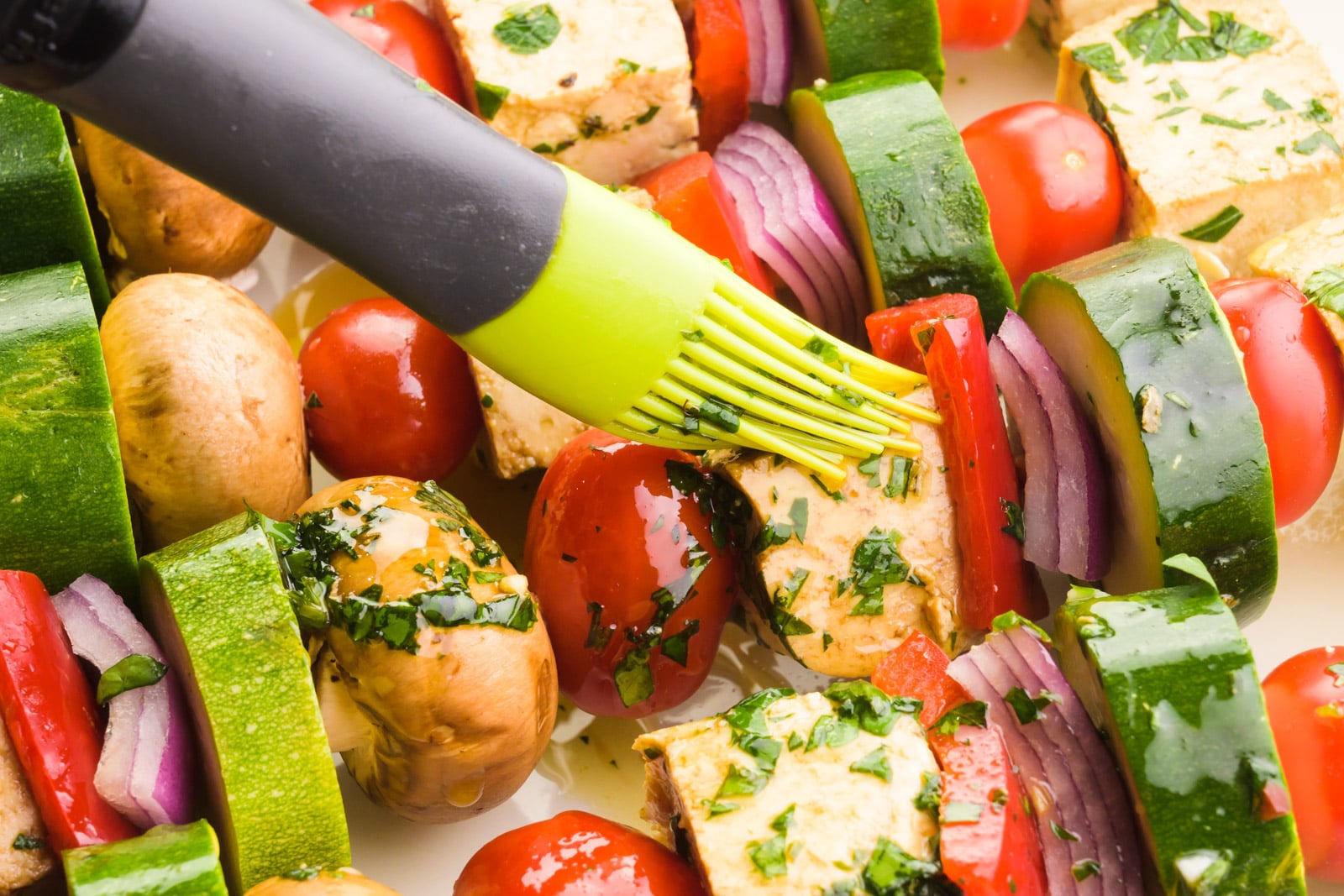 Vegan kebabs are being brushed with marinade before being placed on the grill.